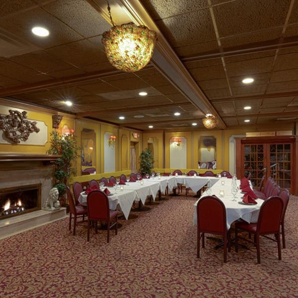 Elegant private dining room with U-shaped table, red chairs, fireplace, and ornate chandeliers.