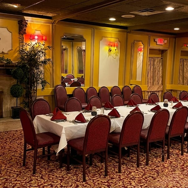 A formal dining room with a long table set with white tablecloths and red napkins, and a fireplace.