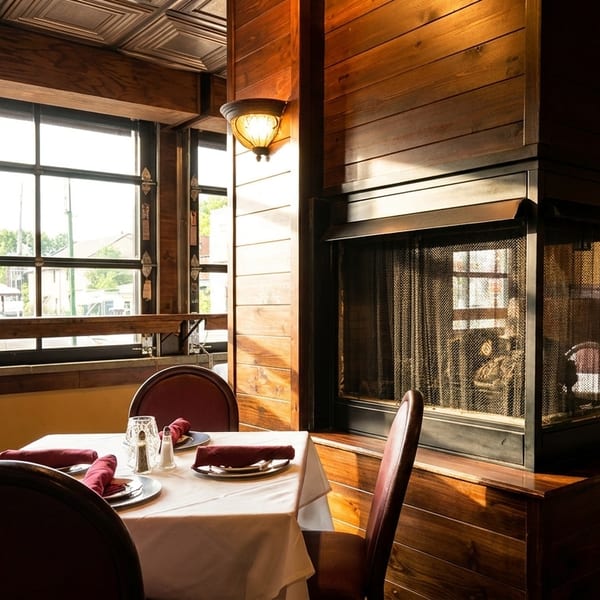 Cozy restaurant interior with a set table, fireplace, large windows, and warm lighting.