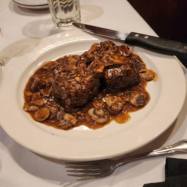 Two pieces of steak covered in mushroom gravy on a white plate with silverware and a wine glass.