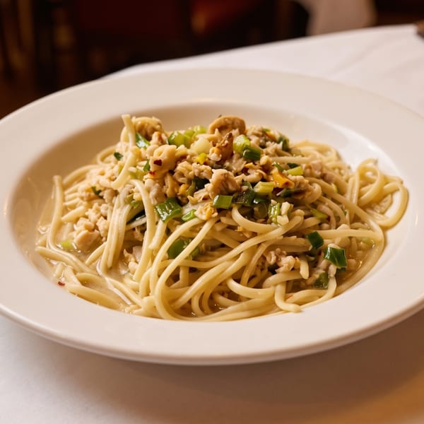 A white bowl of spaghetti with clams, green onions, and a light sauce on a white tablecloth.